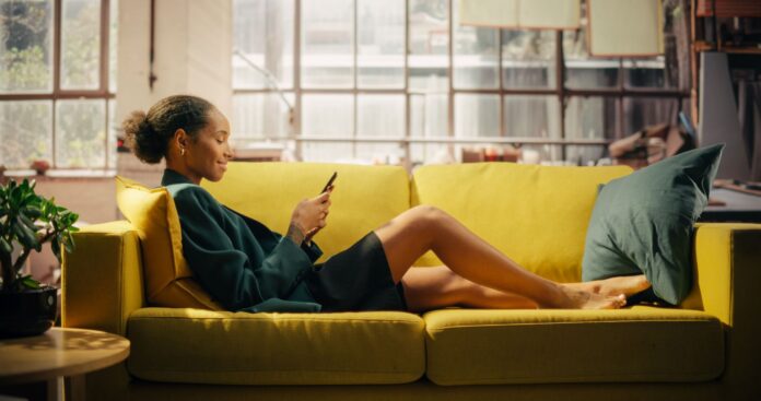 Happy Smiling African American Woman Relaxes on Sofa, Using Smartphone for an Online Shopping Social Media Browsing, E-commerce, Connectivity